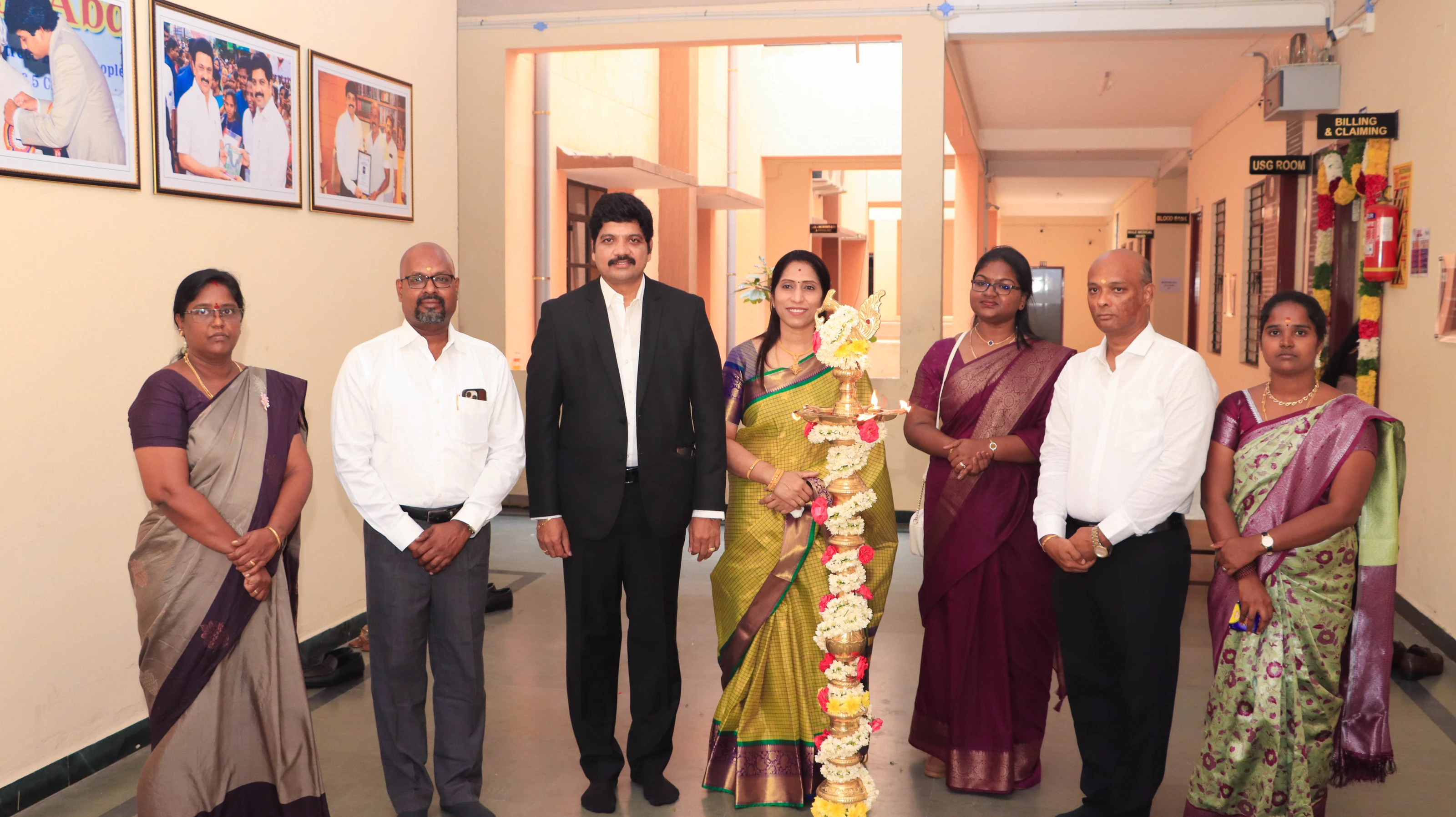 Guests and college staff stand together beside the lit lamp