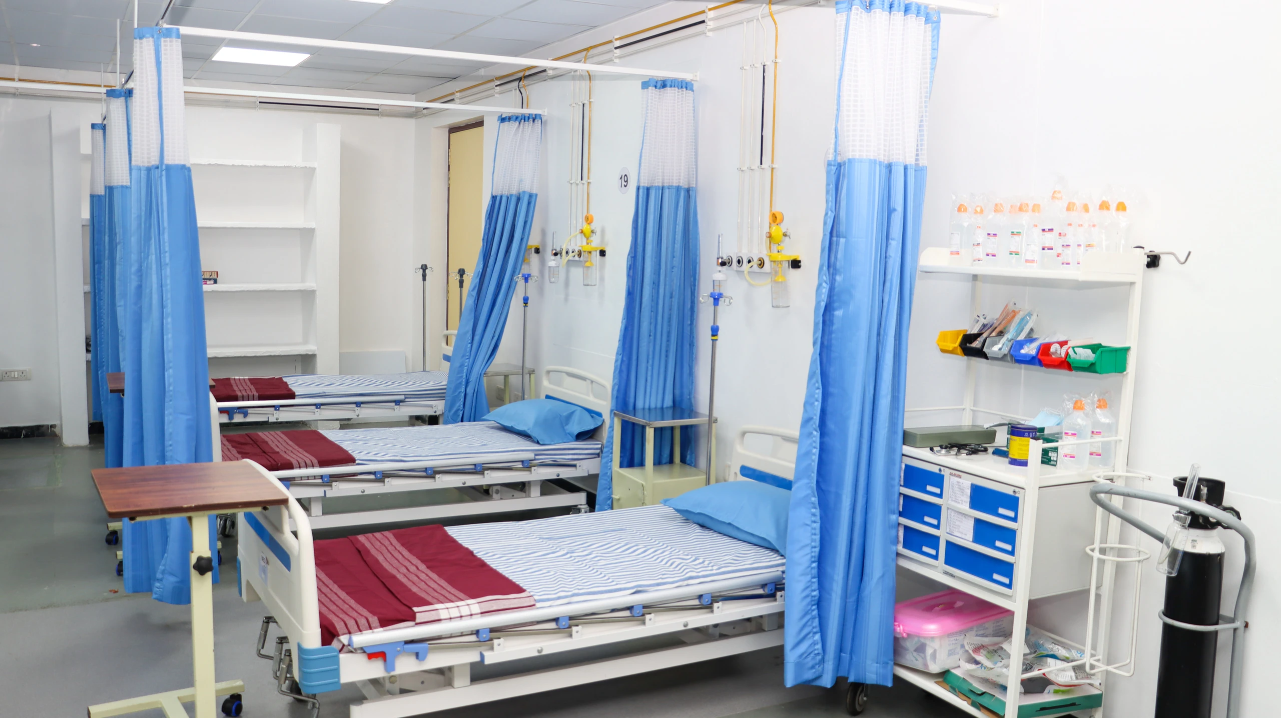 Hospital beds with curtains, an oxygen supply and a supply trolley